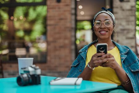 Pretty afro-american woman using smartphone outside cafeの写真素材