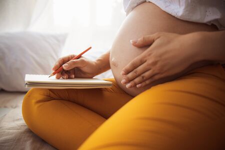 Pregnant young woman writing in spiral notebookの写真素材