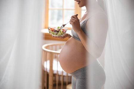Smiling pregnant woman eating fresh salad at home