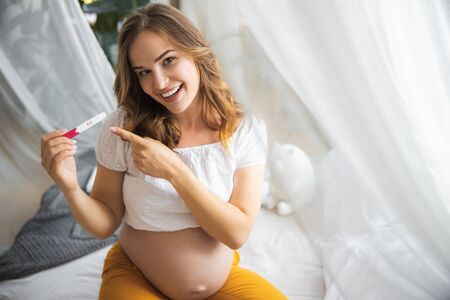 Happy pregnant lady pointing at positive results of pregnancy test
