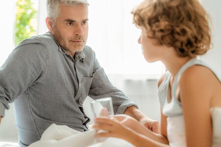 Mature father looking at sick son with pills and waterの写真素材