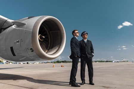 Handsome adult colleagues standing near engine of airplaneの写真素材