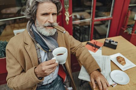 Elegant senior man smoking and drinking coffee at outdoor cafe