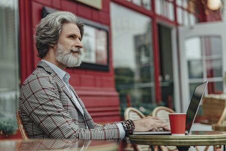 Elegant senior man using laptop at outdoor cafeの写真素材
