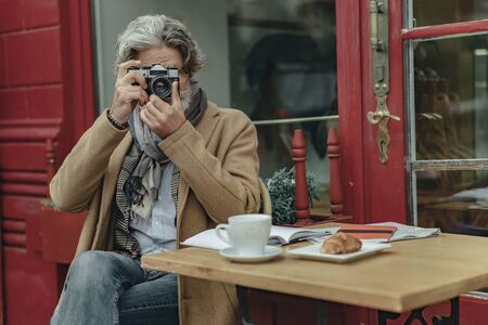 Senior man using retro camera at outdoor cafeの写真素材