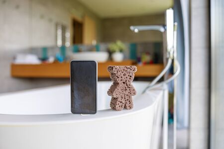 Modern mobile phone and bath sponge on bathの写真素材