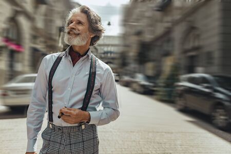 Cheerful senior man with cigar standing on the streetの写真素材