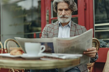 Handsome old gentleman reading newspaper during lunchの写真素材