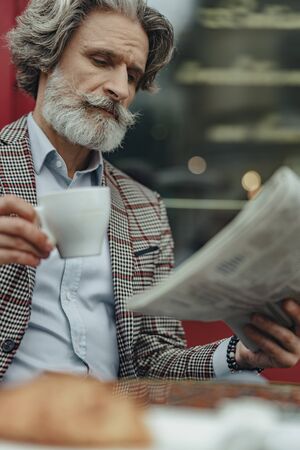 Good-looking senior man reading daily news and drinking coffeeの写真素材