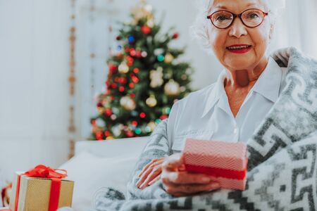 Smiling old female in glasses holding Christmas boxの写真素材