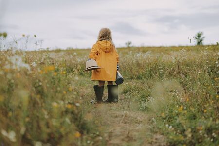 Little girl in raincoat is holding hat outdoorsの写真素材