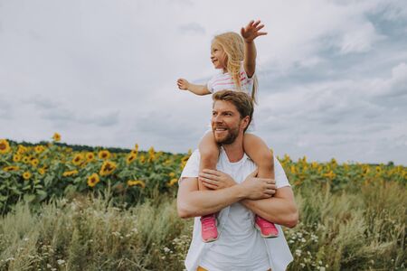 Happy cheerful daughter sitting on her smiling dads shoulders outdoorsの写真素材