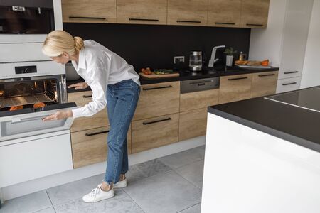 Adult woman is standing near the ovenの写真素材