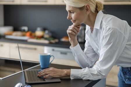 Smiling adult woman is looking on screenの写真素材