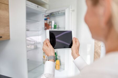 Woman is using tablet to managing fridgeの写真素材
