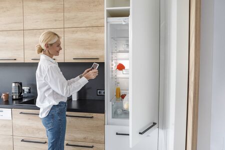 Happy adult woman is standing near fridgeの写真素材