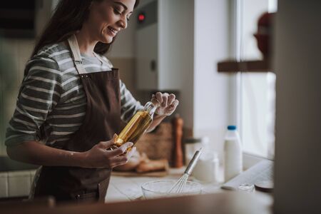 Joyful woman is pouring oil to dishの写真素材