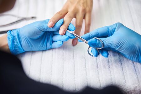 Manicure master removing cuticle on lady hand with scissors