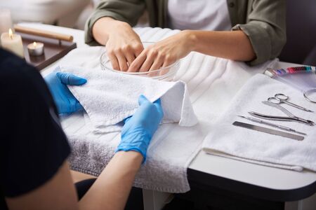 Young lady soaking hands in nail bath while manicurist holding soft towelの写真素材