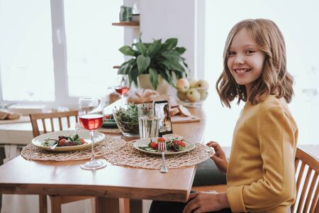 Cute little girl in yellow sweater having dinner at homeの写真素材