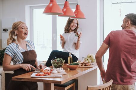 Cute little girl taking photo of father while her mom cooking dinnerの写真素材