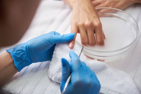 Young lady soaking hand in nail bath while manicurist holding her little finger