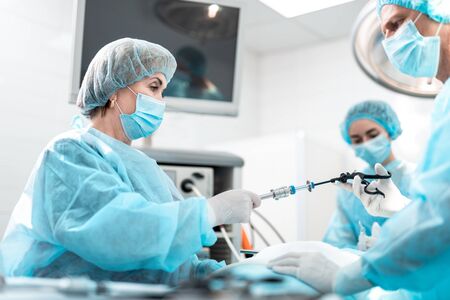 Nurse in protective mask giving laparoscopic instrument to surgeonの写真素材