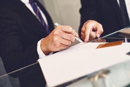 Young man signing the document and his business partner pointing to it