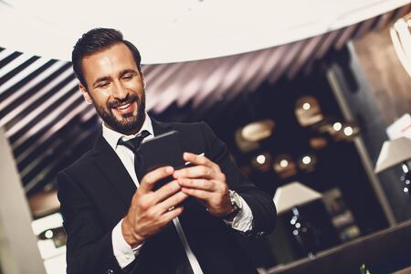 Bearded man standing alone and looking at the screen of his modern smartphone