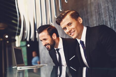 Smiling man looking at the laptop while his colleague standing nearの写真素材