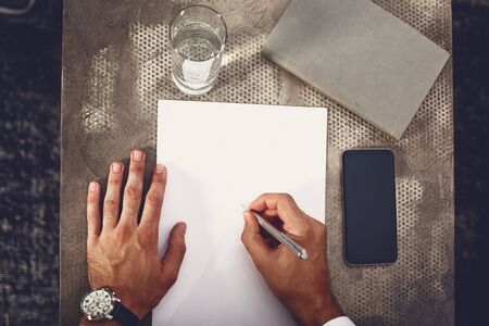 Top view of young man making notes on the sheet of paper