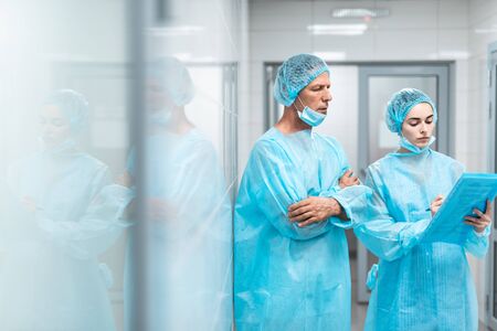 Young doctor making notes and her colleague looking