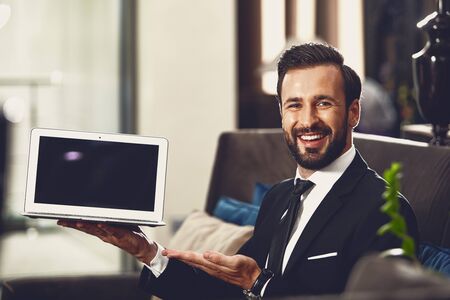 Excited young man smiling while demonstrating his laptopの写真素材