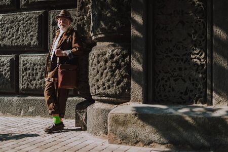 Hipster cheerful old man leaning against buildingの写真素材