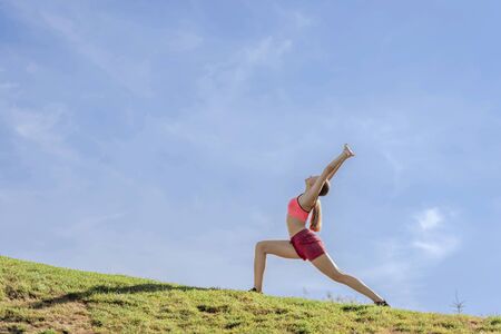 Young lady doing yoga practice on green hill