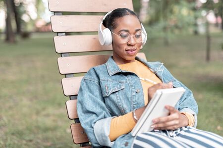 Merry girl with sketchbook and earphones in park stock photo