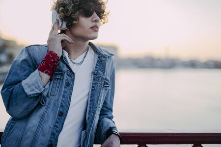 Curly young man in earphones near river stock photoの写真素材