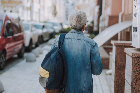 Back view of a senior lady with a backpack walking along the sidewalk
