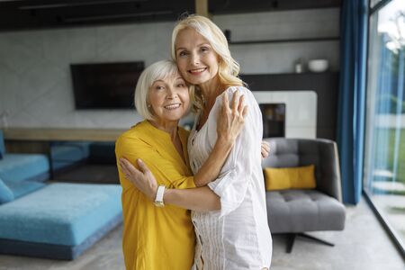 Happy adult mother and daughter hugging at homeの写真素材