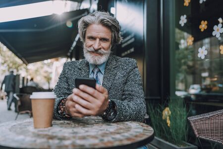 Smiling adult man is looking on smartphoneの写真素材