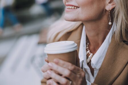 Smiling lady is holding hot drink on the streetの写真素材
