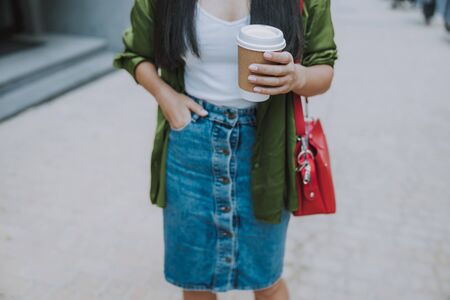 Young female is holding hot drink on the streetの写真素材