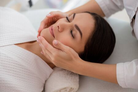 Masseuse massaging lady face at beauty salonの写真素材