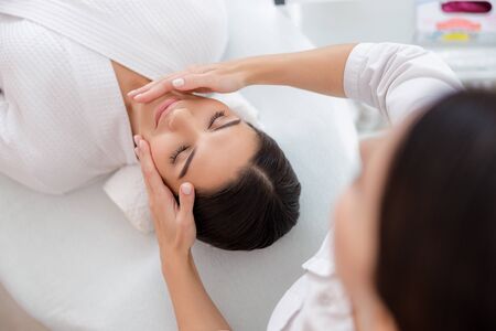 Masseuse hands massaging face of young ladyの写真素材