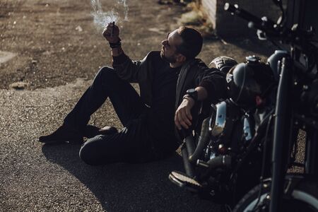 Handsome biker sitting near motorbike and smokingの写真素材