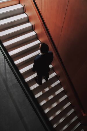 Top view with focus on back of attractive man standing on steps indoors. He is wearing elegant suit while moving upstairsの写真素材