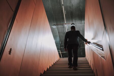 Low angle focus on executive in classic suit. He is walking on steps to office. Copy space in left...