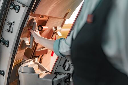 Young stewardess opening vehicle door in airplane stock photo. Airways concept
