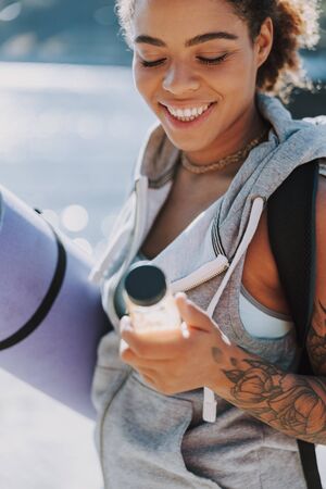Cheerful Afro American lady holding yoga mat and bottle of juiceの写真素材
