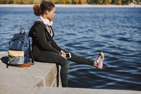 Afro American lady with smartphone sitting by the river
